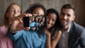 Four diverse multiethnic millennial friends showing spectator selfie on smartphone