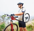 Taking his bike over some bumpy terrain. a sportsman carrying his mountain bike.