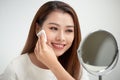 Taking off her make-up. Beautiful cheerful young woman using cotton disk and looking at her reflection in mirror with smile while Royalty Free Stock Photo