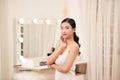 Taking off her make-up. Beautiful cheerful young woman using cotton disk and looking at her reflection in mirror with smile while Royalty Free Stock Photo