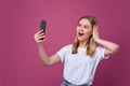 Taking picture. cheerful blond-haired woman doing selfie on isolated pink background