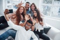 Taking a picture. Cheerful young friends having fun and drinking in the white interior