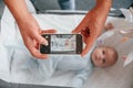Taking picture by smartphone. Father with his newborn baby is indoors. Conception of single dad Royalty Free Stock Photo
