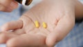 Two small bright yellow cylindrical pill capsules fall into palm of hand from pill bottle. Close-up, front view, center