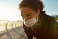 Taking a rest. Close up photo of exhausted african female jogger in medical mask resting after run while standing on the