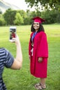 Taking a smartphone photo of a recent high school graduate in her cap and gown Royalty Free Stock Photo