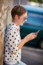 Taking social media by storm. a trendy young woman using her phone while leaning against a wall outside.