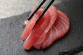 Taking tasty sashimi (piece of fresh raw tuna) from black board, closeup
