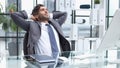 Cheerful young man holding hands behind head and keeping eyes closed while sitting at his working place Royalty Free Stock Photo