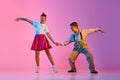 Talented, artisitc children, boy and girl in retro clothes dancing lindy hop against pink studio background in neon