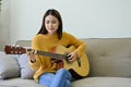 Talented Asian female musician or guitarist playing her acoustic guitar in her living room Royalty Free Stock Photo