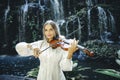Talented Caucasian woman playing violin near waterfall. Music and art concept. Pretty girl wearing white dress in nature. Water Royalty Free Stock Photo