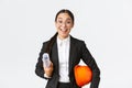 Talented excited asian female architect starting work on construction, holding blueprints and safety helmet, wearing Royalty Free Stock Photo