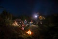 They talk and drink. car and hikers near campfire. Couple man and woman sitting near bonfire under majestic blue sky with stars.