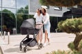 Talking and having fun. Two female friends having a walk with baby carriage outdoors Royalty Free Stock Photo