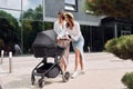 Talking and having fun. Two female friends having a walk with baby carriage outdoors Royalty Free Stock Photo