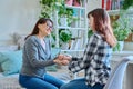 Talking mother and teenage daughter sitting together on couch at home, smiling holding hands Royalty Free Stock Photo