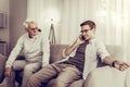 Mature son talking over phone while father sitting on a couch