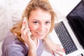 Talking on the smart phone, working on laptop attractive happy smiling young business woman in bed in pajamas Royalty Free Stock Photo