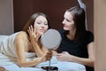 Talking and smiling women beautician and mature female patient with mirror in beauty salon