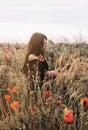 Beautiful young brunette woman in off shoulders black dress sitting in profile in a wild poppies field Royalty Free Stock Photo