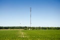 Tall antenna and wind Turbine in a green level field and deep bl