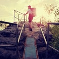 Tall backpacker hold handrail on rock. Sunny daybreak in rocks. Hiker with big backpack, baseball cap, dark pants and white shirt Royalty Free Stock Photo