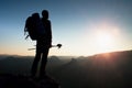 Tall backpacker with poles in hand. Sunny hike day in rocky mountains. Hiker with big backpack stand on rocky view point above mis Royalty Free Stock Photo