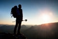 Tall backpacker with poles in hand. Sunny hike day in rocky mountains. Hiker with big backpack stand on rocky view point above Royalty Free Stock Photo