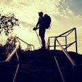 Tall backpacker with poles in hand. Sunny spring daybreak in rocky mountains. Hiker with big backpack, baseball cap, pants and Royalty Free Stock Photo