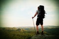 Tall backpacker with poles in hand. Sunny summer evenng in rocky mountains. Hiker with big backpack stand on rocky view point Royalty Free Stock Photo