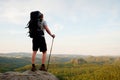 Tall backpacker with poles in hand. Sunny summer evenng in rocky mountains. Hiker with big backpack stand on rocky view point Royalty Free Stock Photo