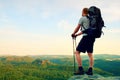 Tall backpacker with poles in hand. Sunny summer evenng in rocky mountains. Hiker with big backpack stand on rocky view point abov Royalty Free Stock Photo