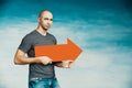 A tall bald man in a gray T-shirt and blue jeans holds in his hands a pointer in the form of an arrow pointing to the right and lo Royalty Free Stock Photo