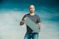 A tall bald man in a gray T-shirt and blue jeans holds in his hands a pointer in the form of an arrow pointing to the side Royalty Free Stock Photo