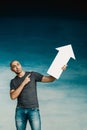 A tall bald man in a gray T-shirt and blue jeans holds in his hands a pointer in the form of an arrow pointing to the up and smile Royalty Free Stock Photo