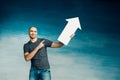 A tall bald man in a gray T-shirt and blue jeans holds in his hands a pointer in the form of an arrow pointing to the up Royalty Free Stock Photo