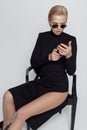 Tall beautiful blonde girl in a black elegant dress in sunglasses on a black chair in the studio on a white background Royalty Free Stock Photo