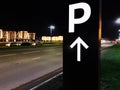 Tall black and white PARKING sign with an up arrow on the side of road at night