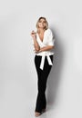 Tall blonde slim woman model in office pantsuit shirt and pants stands with her legs crossed and smiles Royalty Free Stock Photo