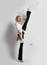 Tall blonde slim woman model in shirt and pants with fan of dollars cash in hand doing vertical splits holding leg up