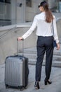 Tall brunette woman in black pants carrying her big suitcase