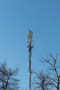 Tall cell tower with many antennas against the blue sky and tree branches