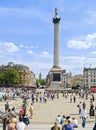 Tall corinthian style Nelson`s Column in Trafalgar Square with people enjoying summer day in city