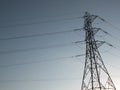 Tall electricity pylon with multiple high voltage cables silhouetted against a blue sky