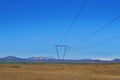 Tall electricity pylons leading high electric current with a high mountains and blue sky in the background in Iceland