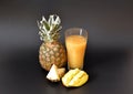 A tall faceted glass of fruit juice on a black background, next to a ripe pineapple and mango pieces Royalty Free Stock Photo