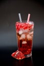 A tall faceted glass of pomegranate juice with ice and seeds on a black background, next to a piece of ripe fruit Royalty Free Stock Photo