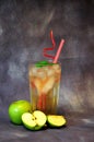 Tall glass of apple nectar with ice and ripe green fruits nearby on a gray background Royalty Free Stock Photo