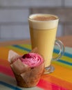Chai latte made with dairy free milk , with vegan cupcake with pink icing in the foreground. Served on a colourful glass platter.